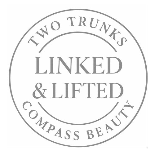 Circular logo with text 'Two Trunks Linked & Lifted Compass Beauty' on a white background